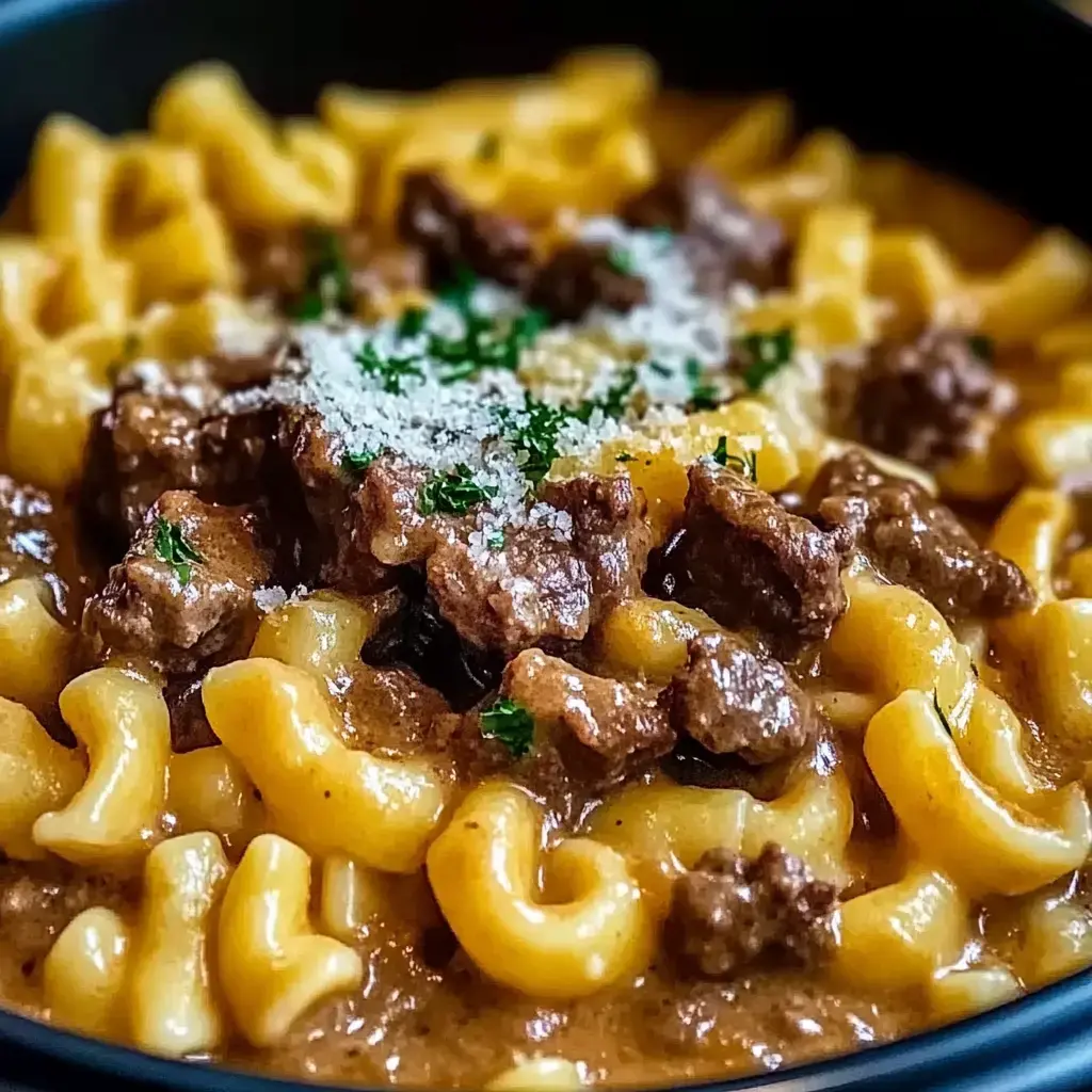 Vista cercana de un plato de pasta cremosa con fideos ondulados, trozos de carne tierna, y una pizca de queso rallado con perejil encima.