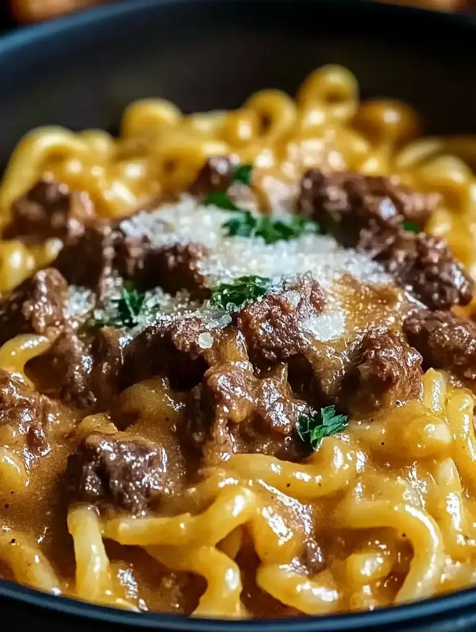 Un plato hondo con pasta enrollada, trocitos de carne, parmesano y perejil encima, todo servido en un bol oscuro.