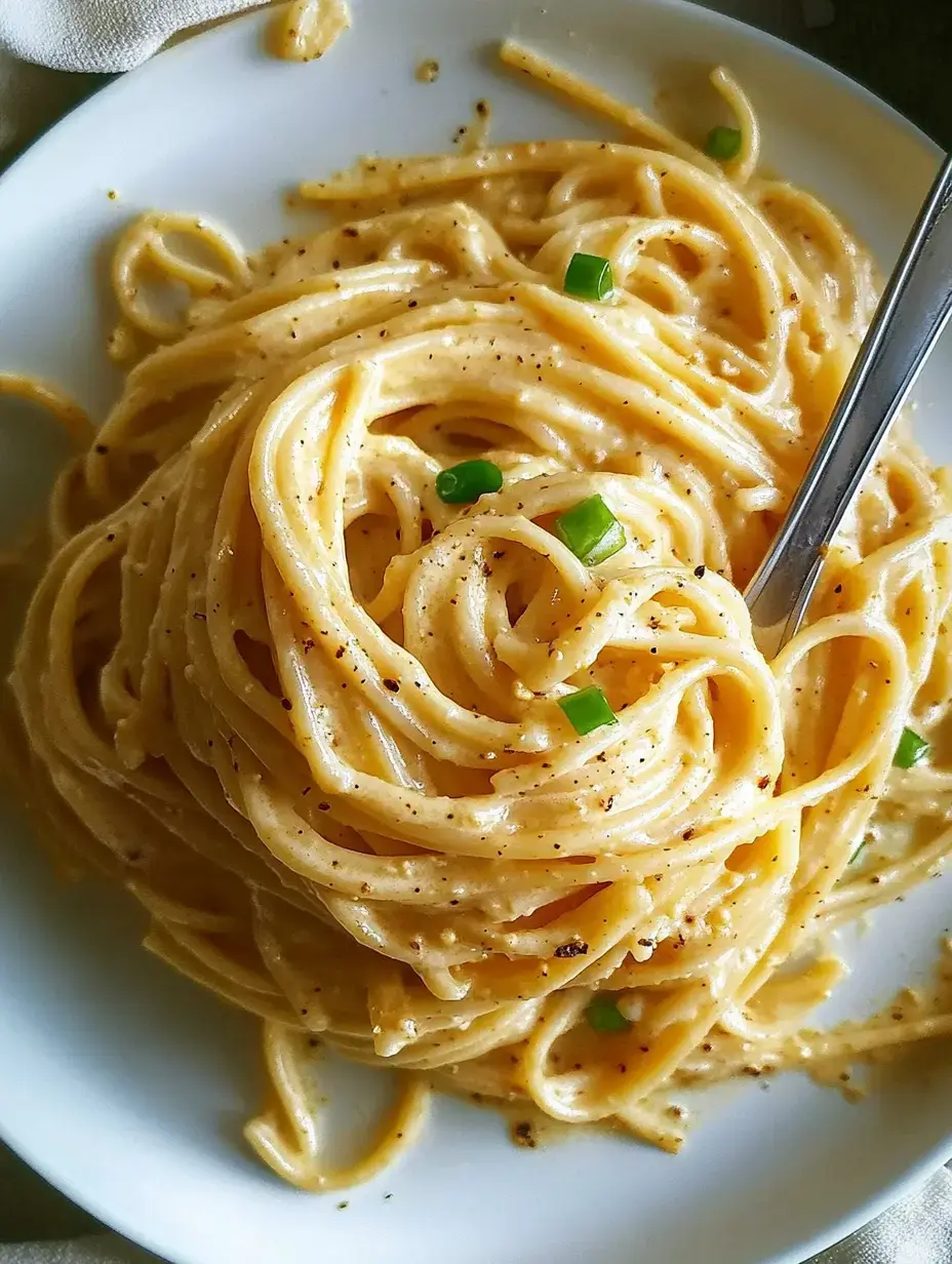 Plato de pasta cremosa con cebollino picado encima y tenedor al lado.