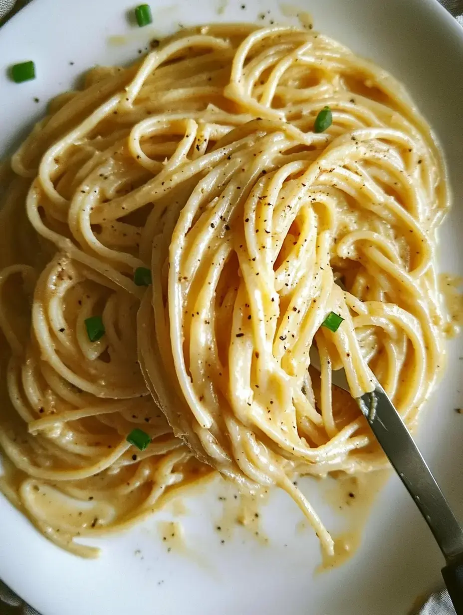 Plato de pasta cremosa decorada con pimienta negra y cebollino picado.