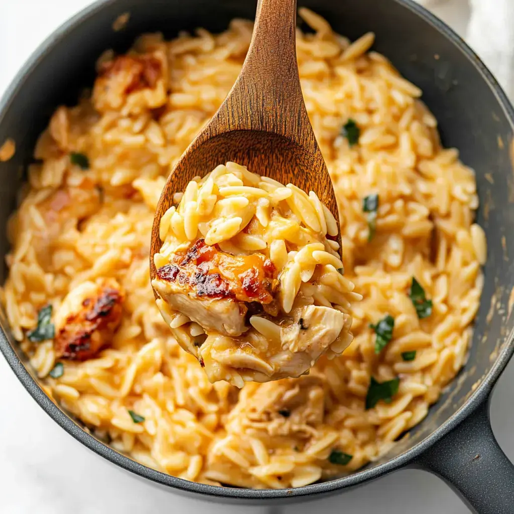 Una cuchara de madera sacando una porción de pasta orzo cremosa con trozos de pollo de una olla negra.