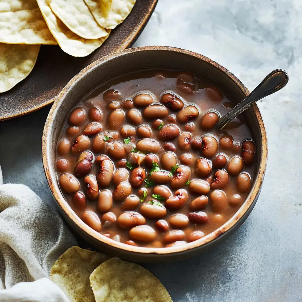 Un tazón de madera lleno de frijoles pintos en caldo, decorado con cilantro picado, junto a un plato de totopos.