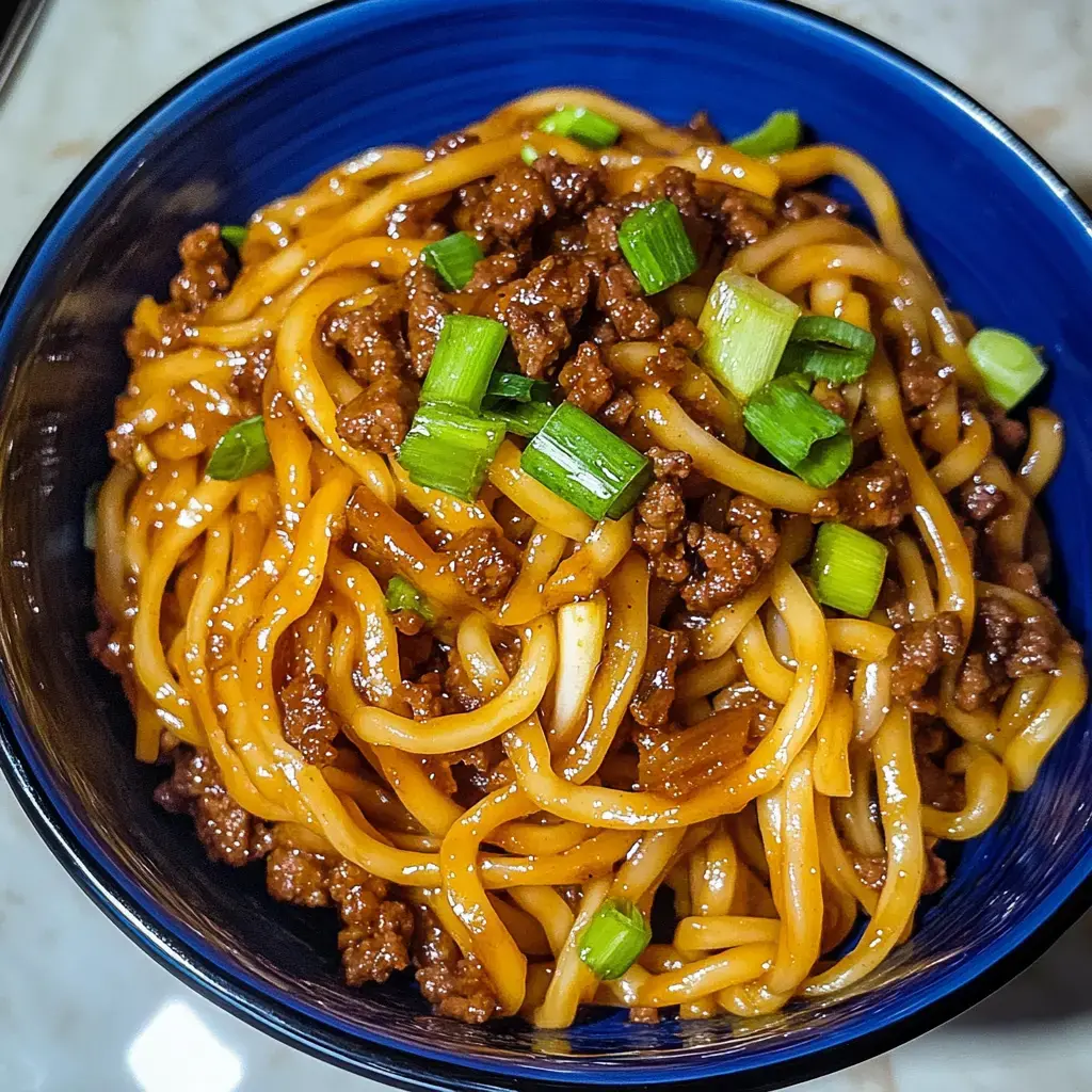 Vista cercana de un plato de fideos con carne molida decorado con cebollín picado.