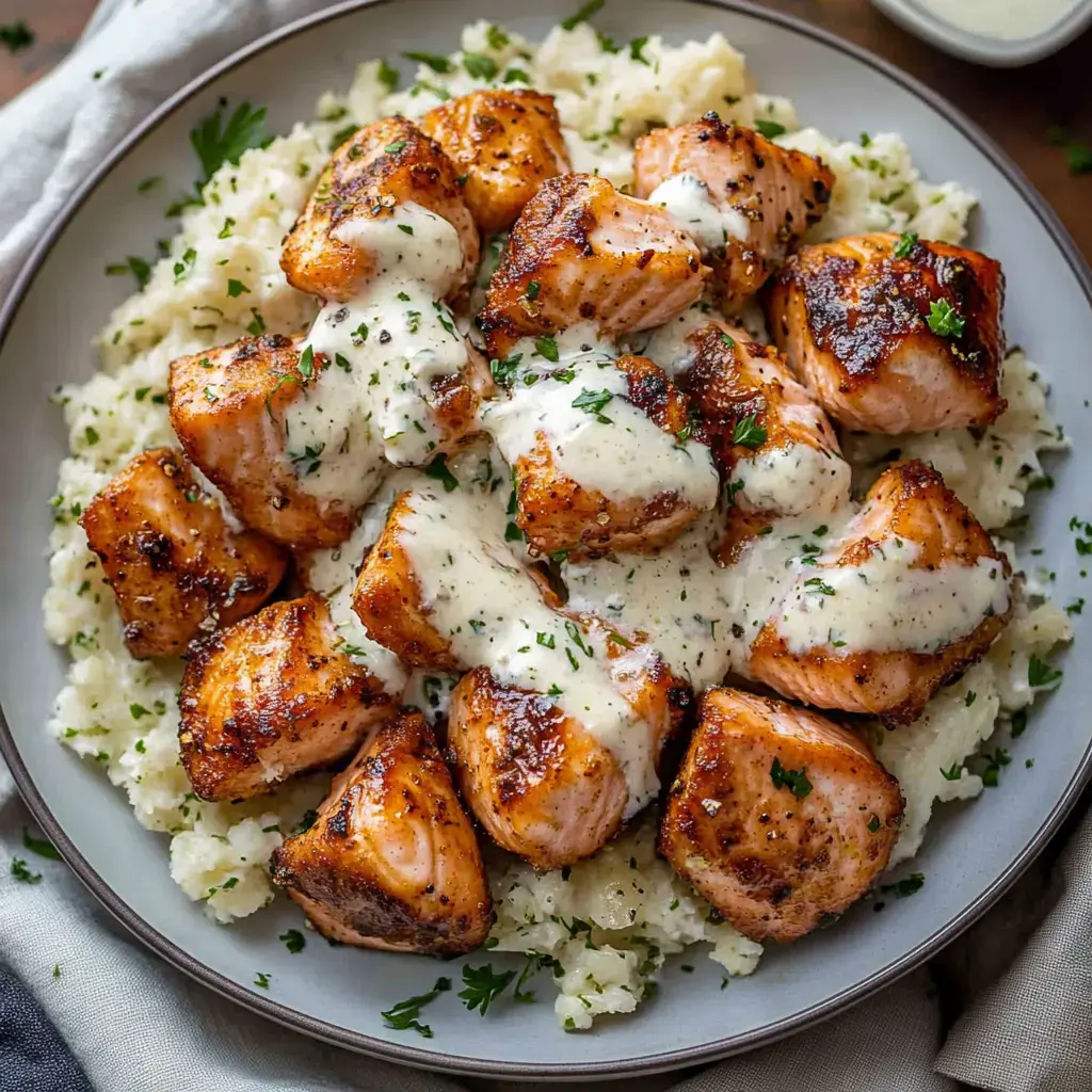 Un plato con trozos de salmón tiernos cubiertos con salsa cremosa, servido sobre arroz esponjoso y decorado con perejil.