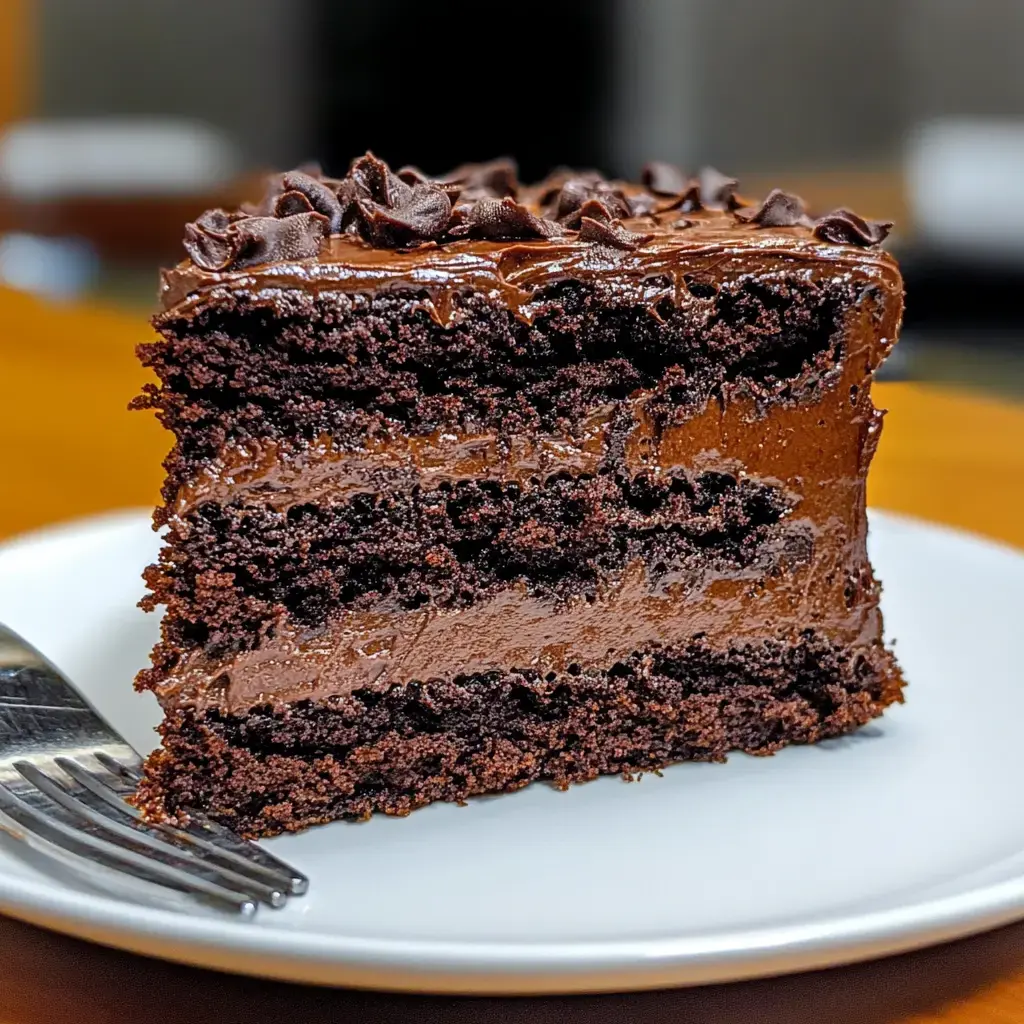 Una porción de pastel de chocolate con capas de crema de chocolate, servido en un plato blanco con un tenedor.