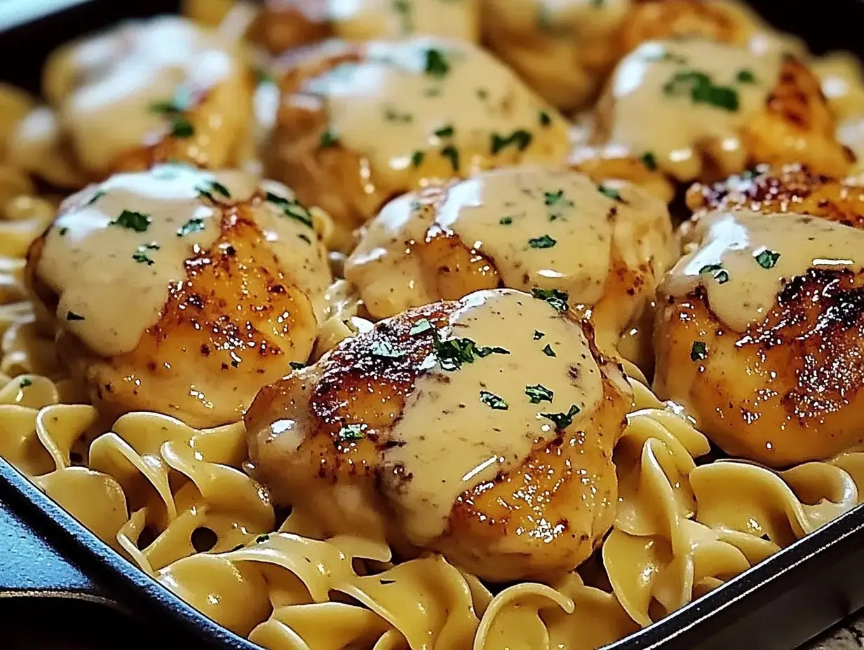 Sartén con fideos de huevo, pollo dorado, salsa cremosa y perejil.