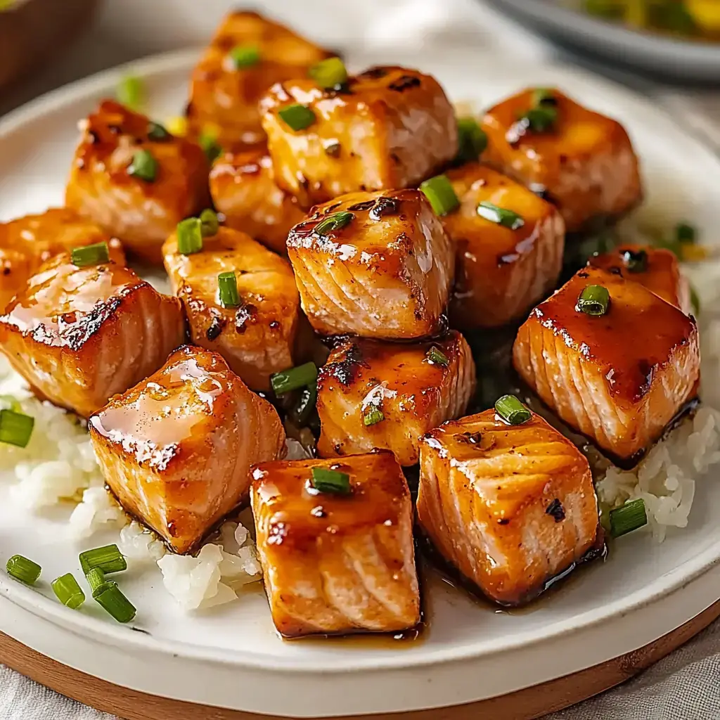 Un plato de cubitos de salmón glaseados con cebollín, sobre arroz.