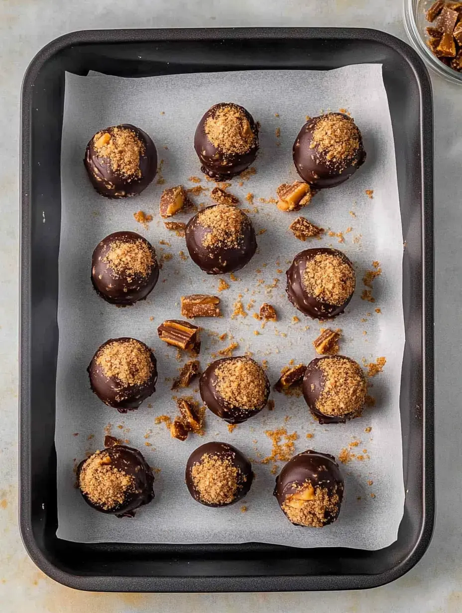 Una bandeja de trufas de chocolate cubiertas de galleta y trocitos de caramelo repartidos.