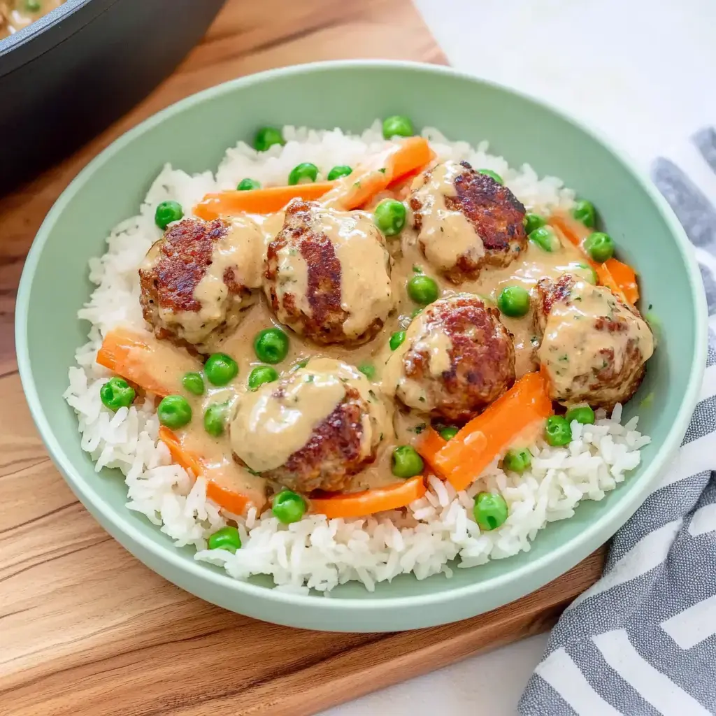 Un plato de arroz con albóndigas en salsa cremosa, decorado con zanahorias y guisantes.