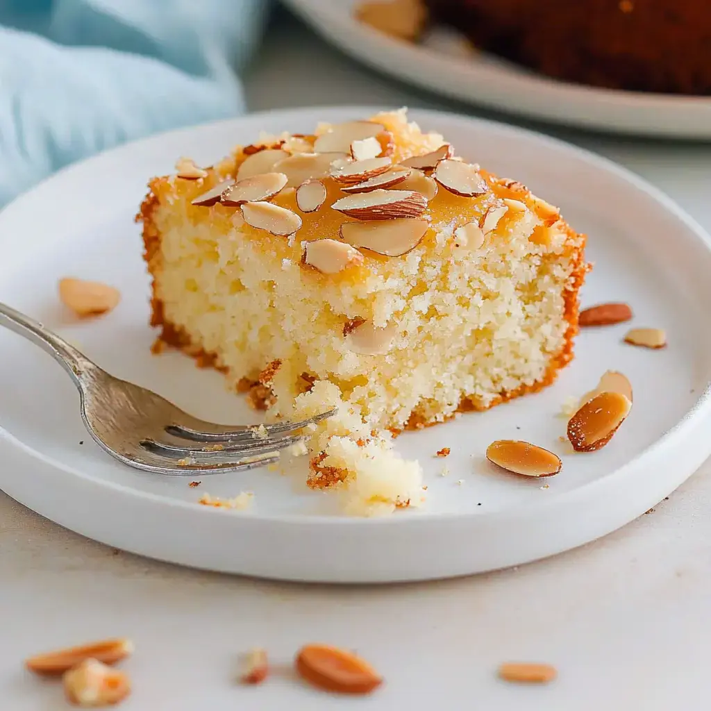 Una rebanada de pastel con almendras sobre un plato blanco, acompañada de un tenedor.