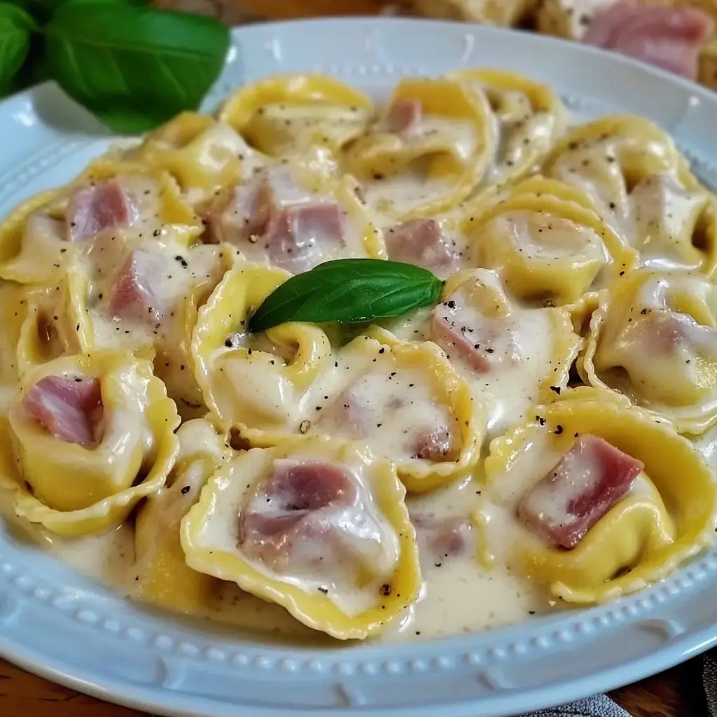 Un plato de tortellini en una cremosa salsa, decorados con una hoja de albahaca fresca.