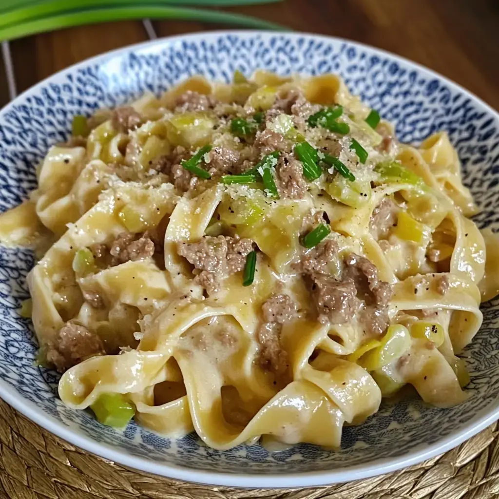 Un plato con pasta en una salsa cremosa, decorado con carne, puerro, cebollino y parmesano.