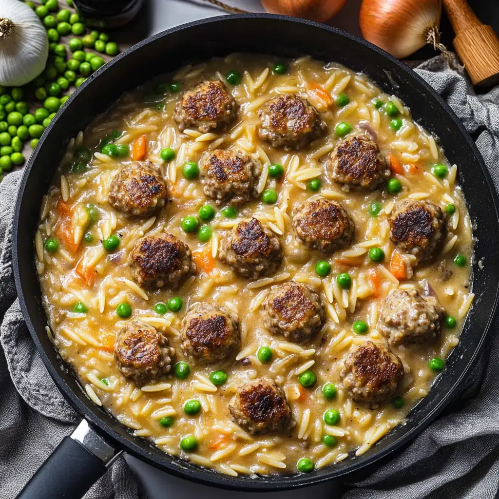 Guiso en sartén con albóndigas, arroz, chícharos verdes y zanahorias en salsa cremosa.