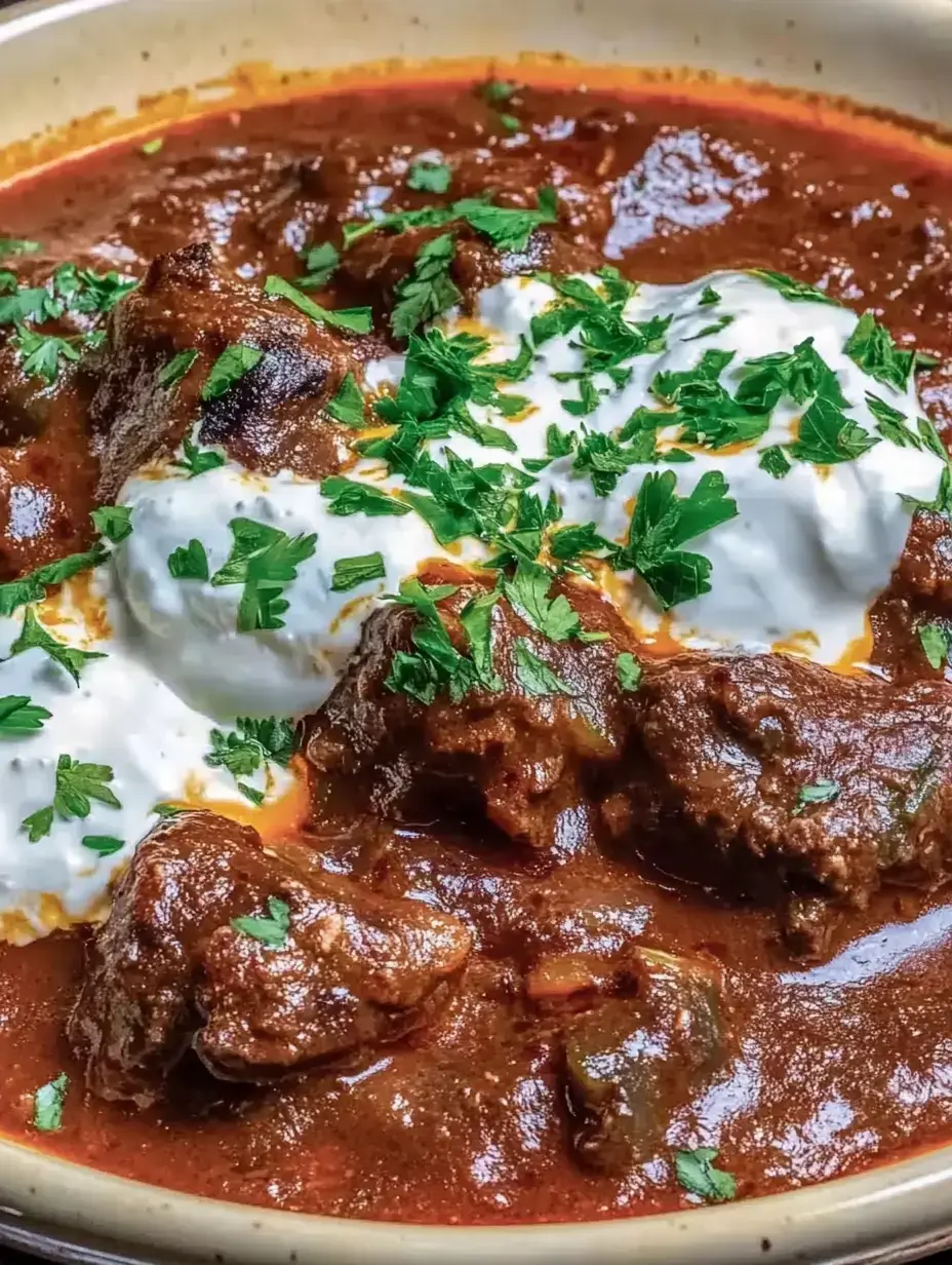 Un platillo jugoso con carne en salsa especiada, decorado con cilantro fresco y un poquito de yogur.